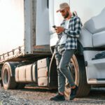 Man leaning on commercial truck looking at his phone.