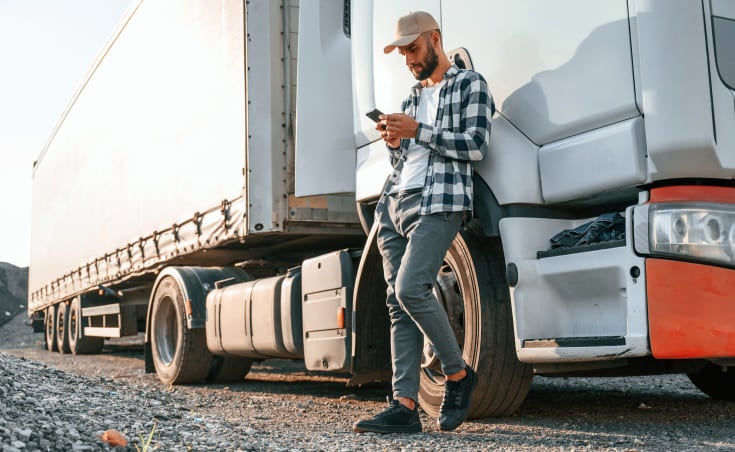 Man leaning on commercial truck looking at his phone.
